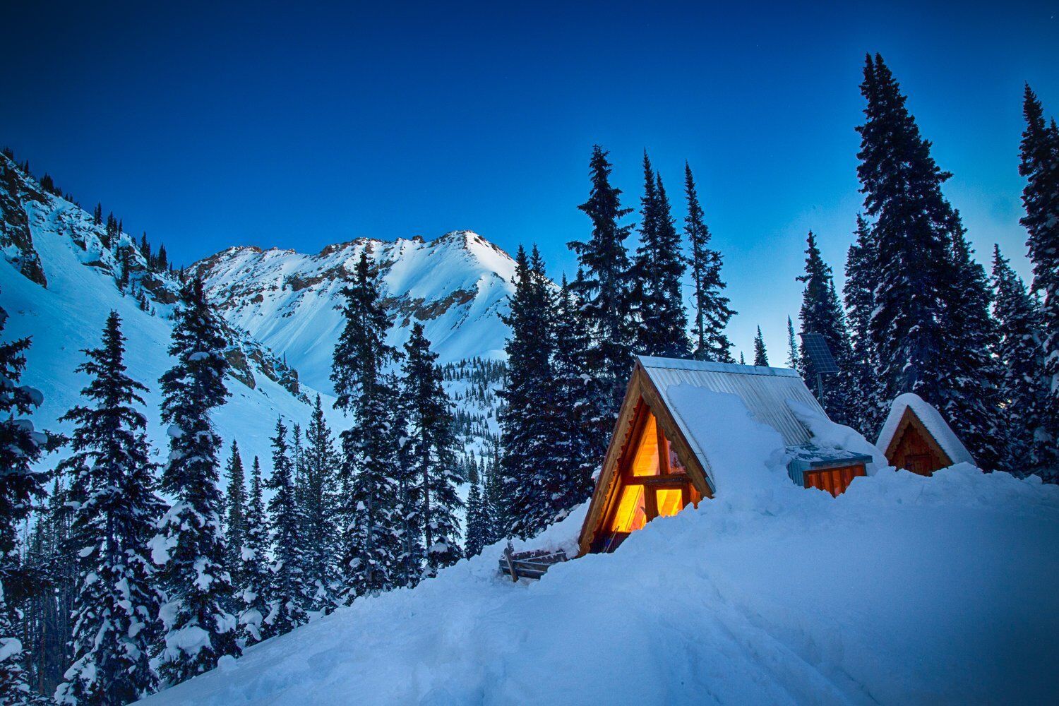 Tagert Hut at dusk, windows lit, deep snow and peaks behind